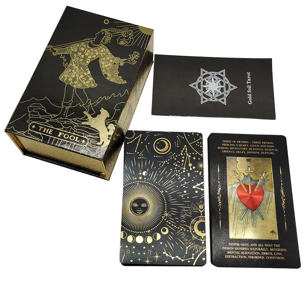 Tarot card deck, showing astrology design in gold on a black background on the back face of a card alongside a case and a booklet