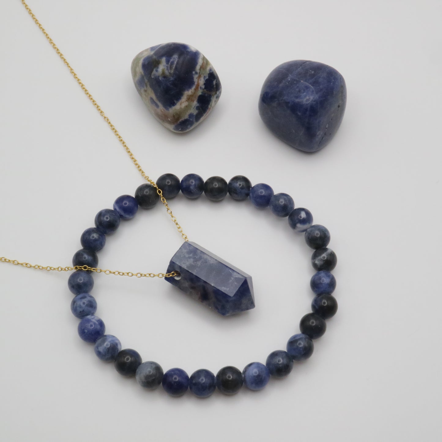 Sodalite Crystal on a fine gold chain surrounded by a Sodalite crystal bracelet and two sodalite tumblestone crystals