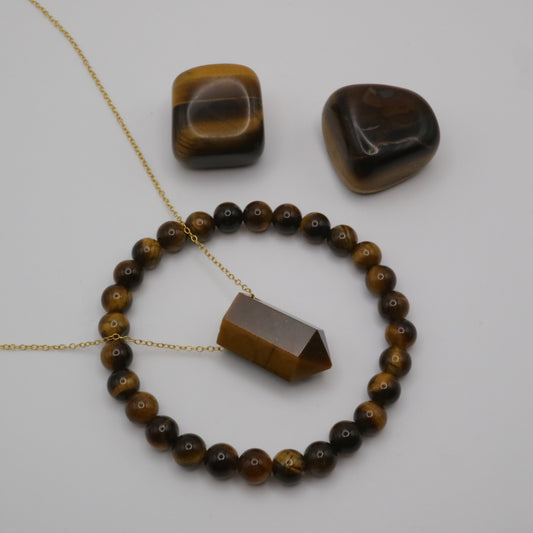 Tiger Eye Crystal on a fine gold chain surrounded by a Tiger Eye crystal bracelet and two Tiger Eye tumblestone crystals