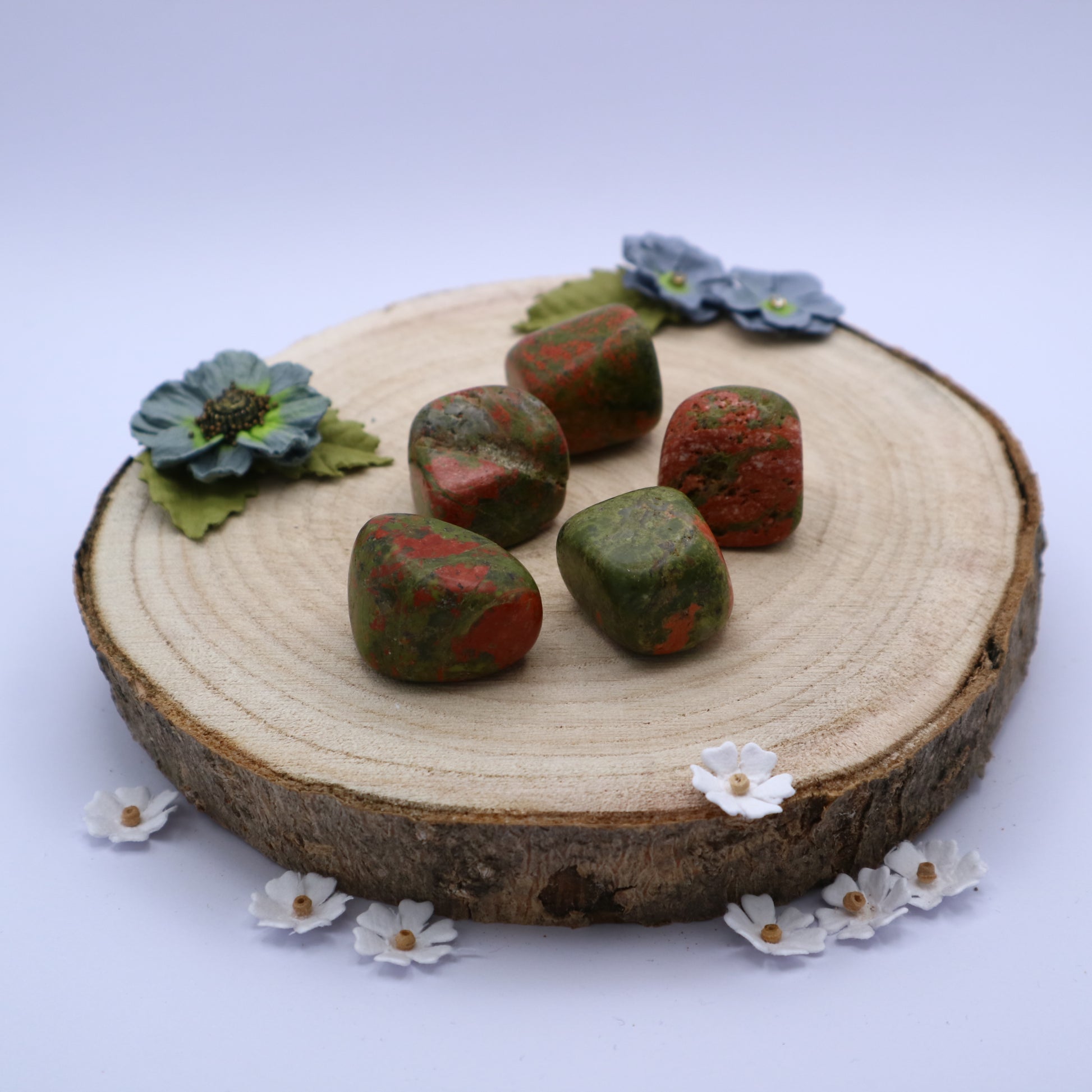 Five pieces of Unakite crystals displayed on a piece of wood surrounded by flowers
