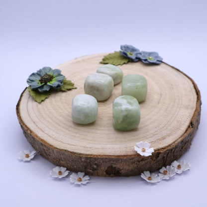Five pieces of New Jade crystals displayed on a piece of wood surrounded by flowers