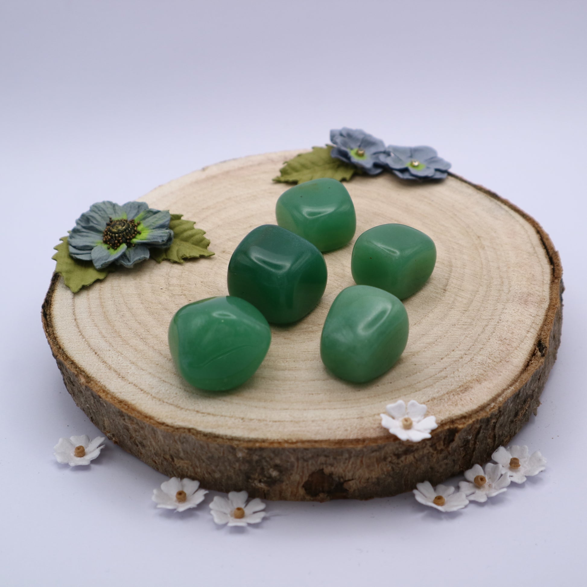 Five pieces of Green Aventurine crystals displayed on a piece of wood surrounded by flowers