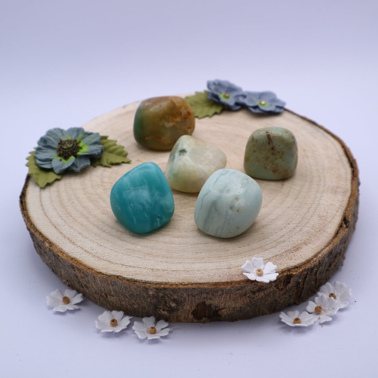 Five pieces of Amazonite crystals displayed on a piece of wood surrounded by flowers