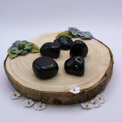 Five pieces of Black Onyx crystals displayed on a piece of wood surrounded by flowers