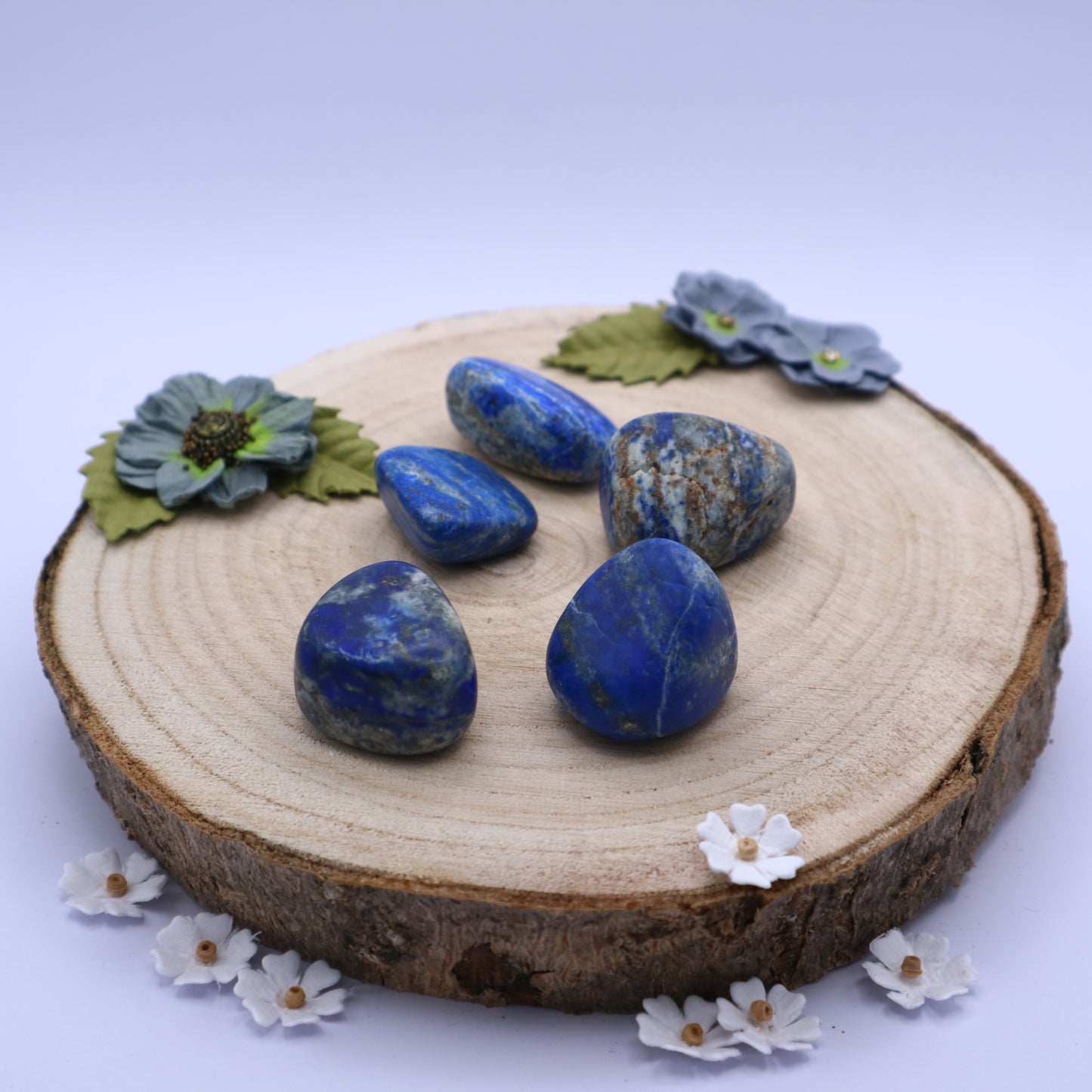 Five pieces of Lapis Lazuli crystals displayed on a piece of wood surrounded by flowers