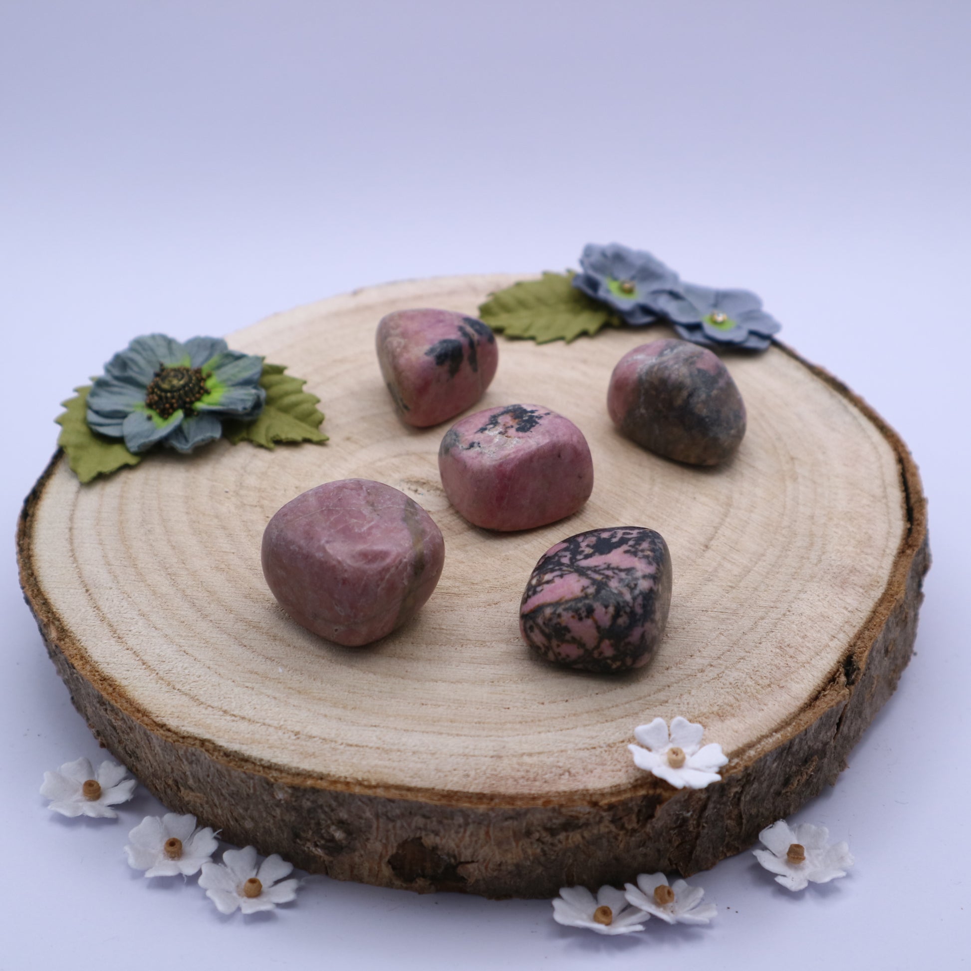 Five pieces of Rhodonite crystals displayed on a piece of wood surrounded by flowers